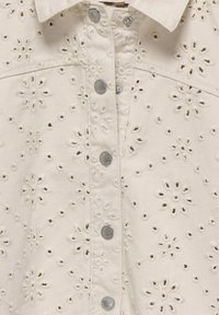 Šviesiai rudos spalvos marškiniai su siuvinėjimais gėlių raštais, su sidabro spalvos kniedėmis ir aklų detalių visame audinyje.