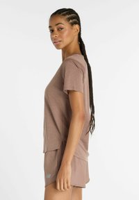 Brown short-sleeve athletic top with a textured pattern, fitted shape, and side slits, paired with matching light brown shorts.