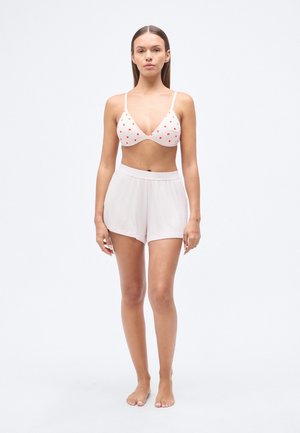 Ensemble soutien-gorge et short. Le soutien-gorge est blanc avec des motifs de cœurs rouges, des bonnets triangulaires et des bretelles fines. Le short est rose clair, en tissu extensible, coupe taille mi-haute.