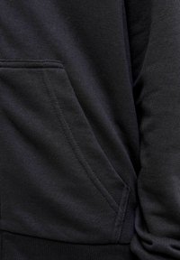 Tissu de sweat à capuche noir avec une texture douce, comportant une poche frontale et des détails de couture visibles, mettant en avant un design classique.