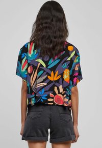 Blusa floreale corta con maniche corte, su sfondo nero, caratterizzata da vivaci stampe botaniche nei colori blu, rosso, arancione e verde.
