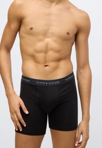 Sorte bomuldsboxershorts med elastisk linning med "TOMMY HILFIGER"-logo i hvidt og rødt. Glat tekstur, tætsiddende design.