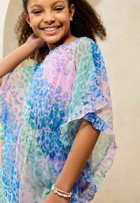 Bunte, durchsichtige Bluse mit einem Leopardenmuster in Blau, Grün und Pink. Rüschenärmel verleihen Textur und verschmelzen lebendige Farben.