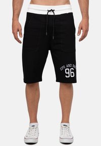 Shorts en coton noirs avec une taille élastique blanche et un cordon de serrage, comportant de grandes poches latérales et portant l'inscription "CIPO AND BAXX 96" en blanc.
