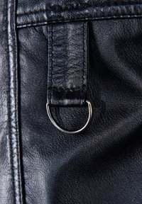 Svart lädermaterial som visar en närbild av en rektangulär rem med en metallring. Ytan är texturerad och slät med synliga stygn.