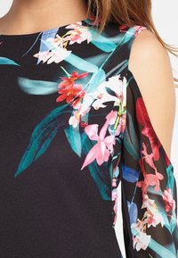 Svart klänning med livliga blommönster i rosa och vitt, med kalla axlar och ett silkeslent, texturerat tyg.