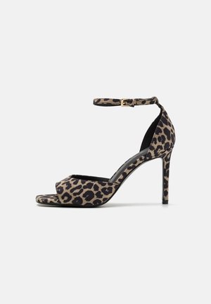 Sandalia de tacón alto con estampado de leopardo, correa en el tobillo y puntera abierta, con un delgado tacón de aguja sobre un fondo blanco liso.