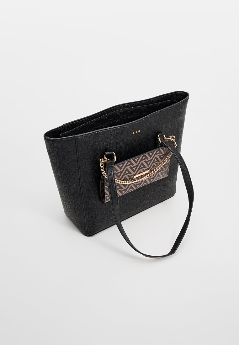 Bolso tote de piel negra texturizada con un bolsillo frontal de patrón geométrico y detalle de cadena dorada, que presenta dos correas largas para llevar.