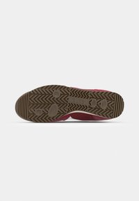 Red athletic shoe with a textured brown rubber sole, featuring a zigzag pattern, circular accents, and a mesh upper for breathability.
