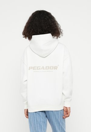 White hooded sweatshirt featuring a large light beige "PEGADOR" logo on the back. The fabric appears soft with a relaxed fit and ribbed cuffs.
