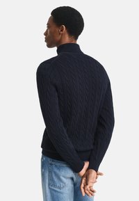 Pulover navy cu guler înalt și tricotaj în carouri, cu manșete și tiv cu nervuri. Prezintă un model texturat și un design ajustat, asortat cu blugi de un albastru deschis.