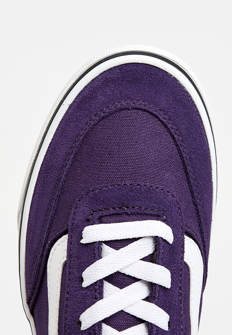 Sneaker in tela viola con lacci bianchi, caratterizzato da una tomaia testurizzata e una suola in gomma con finiture nere lungo il bordo.