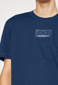 Marineblaues Baumwoll-T-Shirt mit Rundhalsausschnitt und einem gummierten EA7 Emporio Armani-Logo-Patch auf der Brust. Kurzärmlig.