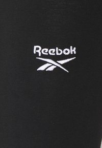 Svarta leggings med en slät textur, med en vit broderad Reebok-logotyp på sidan. Enkel design, inga ytterligare mönster eller dekorationer.