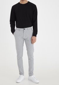 Svart långärmad skjorta i kombination med ljusgrå skräddarsydda byxor, med en framknäppning och sidofickor, fulländad med vita sneakers.