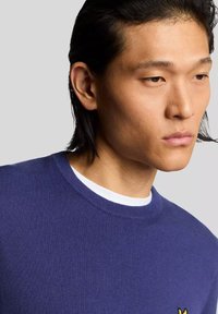 Maglione blu navy con scollo rotondo, realizzato in un tessuto a maglia liscia, caratterizzato da un piccolo logo giallo ricamato sul petto.