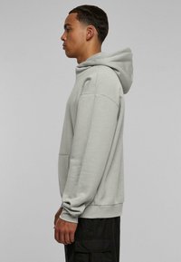 Sudadera con capucha de color gris claro, con bolsillo tipo canguro, textura suave, corte relajado y puños de canalé, vista lateral.