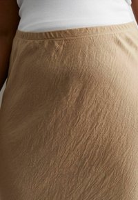 Falda arrugada color tostado con una textura suave y cinturilla elástica, acompañada de una camiseta ajustada blanca.