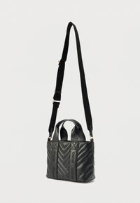 Bolso de mano de cuero negro acolchado con texto en relieve "HUGO", dos asas superiores y correa larga ajustable para el hombro sobre un fondo blanco.