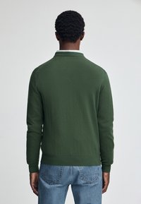 Grön stickad tröja med krage, långa ärmar och ribbad mudd och fåll. Tillverkad av mjukt material, visad från baksidan.