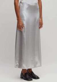 Zilver satijnen maxi rok met een vloeiende textuur, voorzien van een tailleband en gecombineerd met zwarte leren loafers.