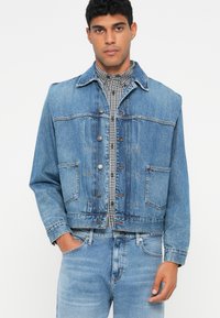 Ανοιχτού μπλε τζιν μπουφάν με κουμπιά, δύο μπροστινές τσέπες και cropped σχέδιο, επενδυμένο με καρό πουκάμισο.