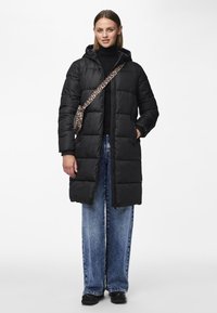 Cappotto lungo imbottito nero con cappuccio, dotato di zip frontale e tasche laterali. Abbinato a jeans in denim azzurro a gamba larga e una borsa con stampa leopardata.