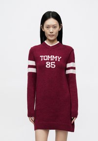Samtrotes Pulloverkleid mit weißem "TOMMY 85"-Aufdruck, V-Ausschnitt, langen Ärmeln und gestreiften Akzenten. Weiche Textur und gerippte Bündchen.