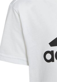 Camiseta blanca de algodón con un gran logo negro. La tela tiene una textura suave, con mangas cortas y un cuello redondo.