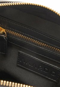 Čierny kožený interiér tašky s použitím zlatého zipsu a obdĺžnikovou visačkou s embosovaným nápisom "AKARDO," predvádzajúci hladkú textúru a čisté línie.