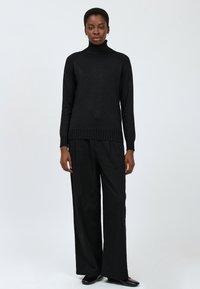 Schwarzer Rollkragenpullover mit geripptem Saum, kombiniert mit weiten schwarzen Hosen. Beide Teile haben eine glatte Textur und eine lockere Passform.