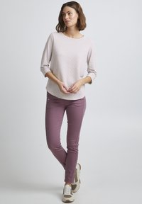 Lichtroze gestreepte langemouwen top met een ronde halslijn, gecombineerd met slim fit paarse broek met zijknopen en sneakers.