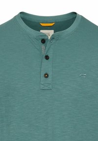 Teal kortærmet henley skjorte lavet af blødt stof med en tre-knaps placket, en subtil tekstur og et lille broderet logo på brystet.