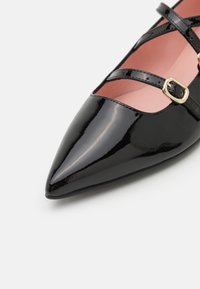 Chaussure plate à bout pointu en cuir verni noir avec deux fines brides et une boucle dorée, doublure intérieure douce rose pâle.
