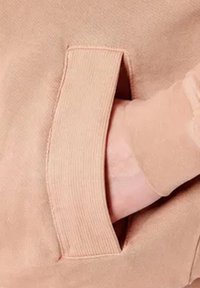 Sudadera rosa claro con un bolsillo rectangular y borde ribeteado. Textura suave con detalles de costura visibles.