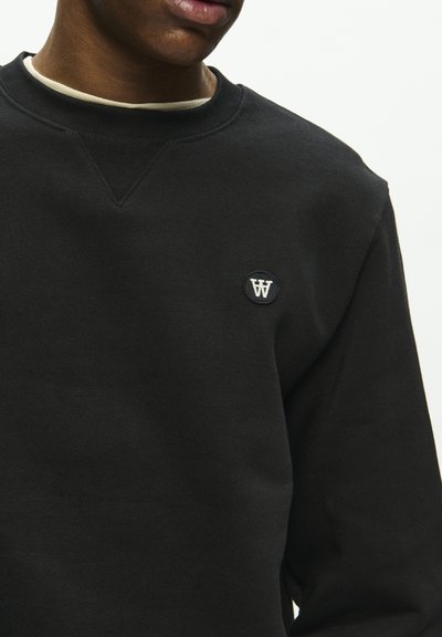 Schwarzer Sweatshirt mit Rundhalsausschnitt, gerippten Bündchen und einem kleinen runden Logo auf der Brust. Der Stoff wirkt weich und strukturiert.