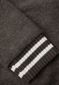 Dunkelbrauner Wollpullover-Bündchen mit einem gerippten Design und weißen sowie hellbraunen horizontalen Streifen. Weiche Textur mit einem leicht fuseligen Erscheinungsbild.