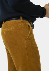 Bruine corduroy broek met een verticale geribbelde textuur, voorzien van een zijzak, een knoopdetail en een zwarte geweven riem.