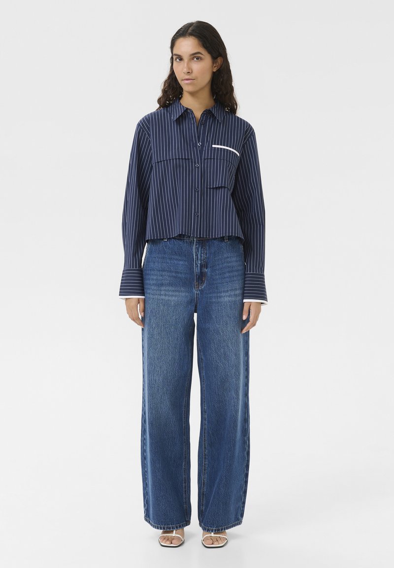 Marine gestreepte cropped t-shirt met lange mouwen, voorzien van een witte borstzak; gecombineerd met wijde blauwe spijkerbroeken.