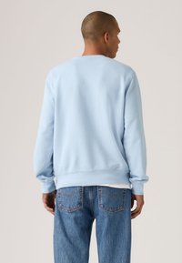 Ανοιχτό μπλε βαμβακερό φούτερ με μακριά μανίκια, ριμπ μανσέτες και στρογγυλή λαιμόκοψη, συνδυασμένο με μπλε τζιν παντελόνι.