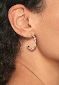 Boucle d'oreille en argent avec un design torsadé, présentant une texture lisse et une finition élégante, portée sur l'oreille d'une personne.
