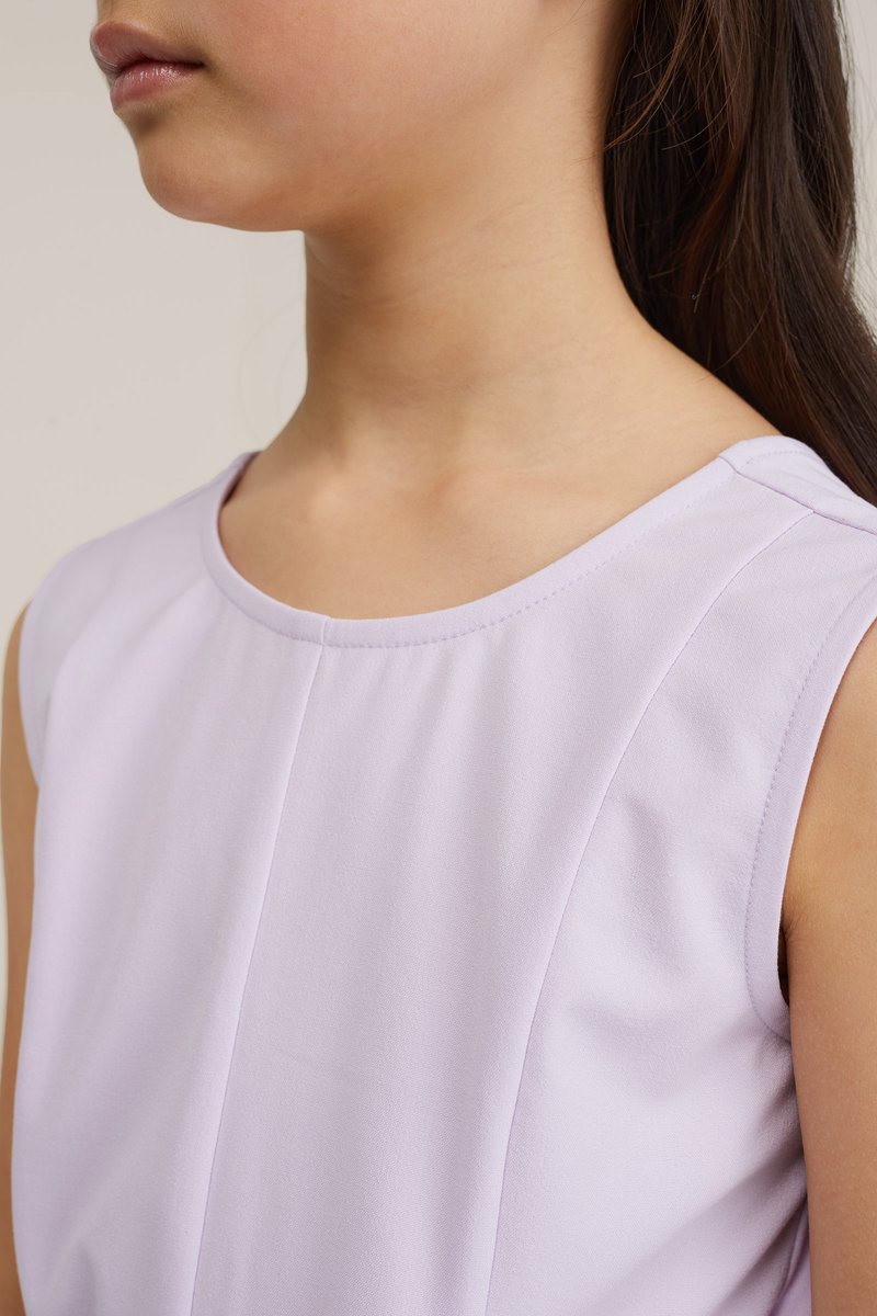 Fiatal személy hosszú, sötét hajjal, ujjatlan világoslila felsőt viselve, a nyaktól a felső mellkasig és a vállig látható.