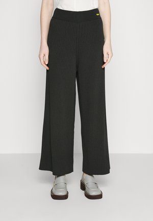 Pantalons à jambes larges et côtelés en gris foncé avec une taille élastique haute. Associés à des mocassins gris avec une semelle blanche contrastante.