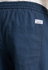 Marineblauwe linnen shorts met een elastische tailleband, voorzien van een achterzak en een label met de tekst "Marc O'Polo Denim." Glad textuur.