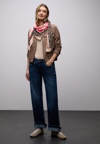 Veste bombardier marron, haut beige, jean bleu oversize et baskets de couleur claire. L'écharpe présente un motif rose et à imprimé animal.