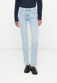 Jeans en denim bleu clair avec une coupe slim et droite, style à cinq poches et décoloration subtile. Associés à des mocassins noirs.