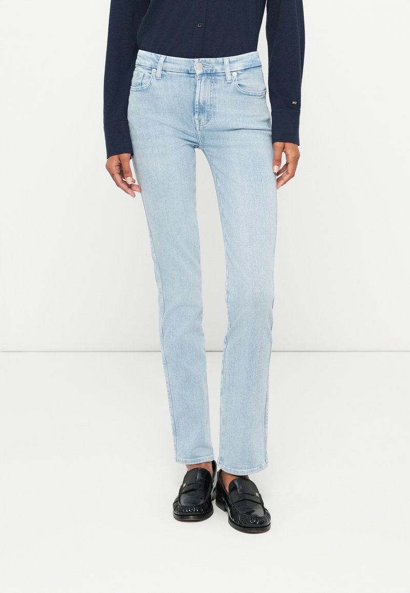 Jeans en denim bleu clair avec une coupe slim et droite, style à cinq poches et décoloration subtile. Associés à des mocassins noirs.
