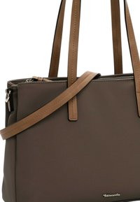 Flätad taupe tote-väska med bruna läderremmar, dragkedjestängning och silverfärgad logodetalj. Slät textur och rektangulär form.