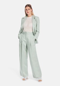 Helles grün gestreiftes Anzug mit einem doppelt geknöpften Blazer und einer weiten Hose, kombiniert mit einem weißen gehäkelten Top und weißen Schuhen.