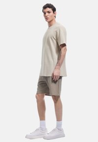 T-shirt in cotone beige chiaro con maniche corte, abbinato a pantaloni corti beige e sneakers bianche. Design semplice, vestibilità comoda, colori solidi.